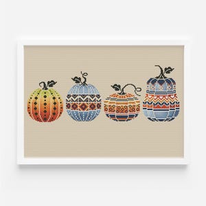 以下が含まれることがあります： オレンジ、ブルー、ブラウンの色合いで、幾何学模様が異なる4つの刺繍されたカボチャ。カボチャはベージュの背景に一列に並んでいます。