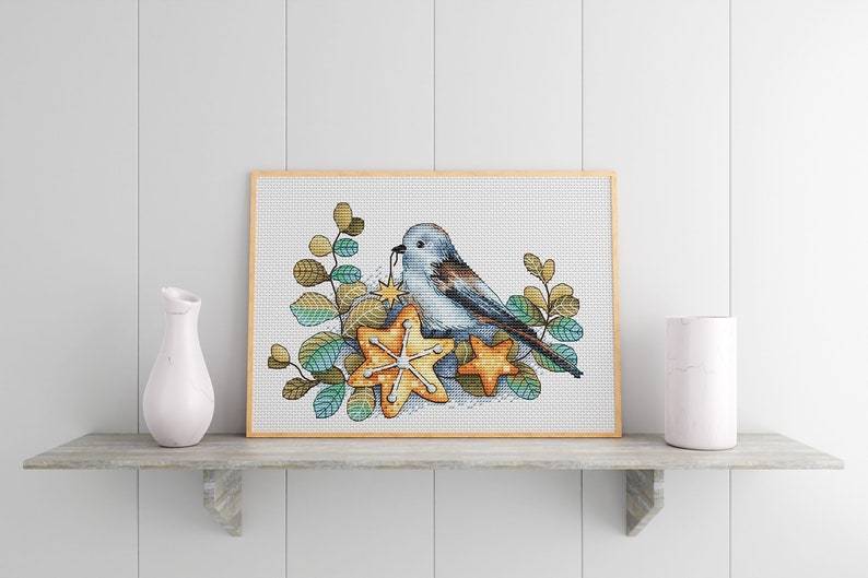May include: A blue bird with brown wings sits on two star-shaped cookies. The bird is holding a small star in its beak. The cookies and bird are surrounded by green leaves.