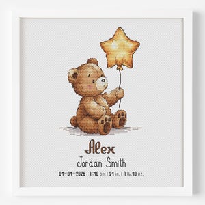 May include: A framed cross-stitch artwork features a brown teddy bear holding a gold star balloon. The bear is sitting down. The name "Alex Jordan Smith" is below the bear, along with the date and time of birth, and measurements: 21 inches and 1 lb. 10 oz.