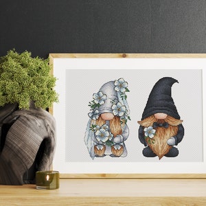 May include: A cross-stitch pattern featuring a bride and groom gnome couple. The bride gnome wears a white dress and veil with blue flowers. The groom gnome wears a black suit with a bow tie and holds a bouquet of blue flowers.