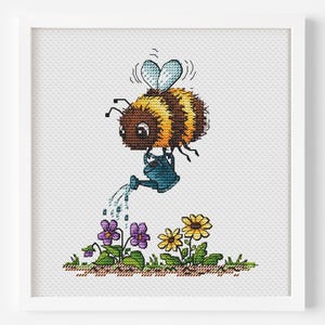 May include: A framed cross-stitch shows a cartoon bee watering flowers. The bee is brown and yellow, holding a blue watering can. Purple and yellow flowers are in the foreground, with green grass and a white background.