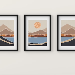May include: Three framed prints of abstract landscape art with a mountain range, a lake, and a sun. The prints are in a minimalist style with a muted color palette of beige, brown, blue, and orange.