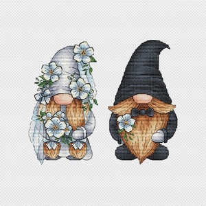 May include: Two gnomes dressed for a wedding. The female gnome wears a white dress with blue flowers and a veil. The male gnome wears a black suit with a bow tie and holds a bouquet of blue flowers.