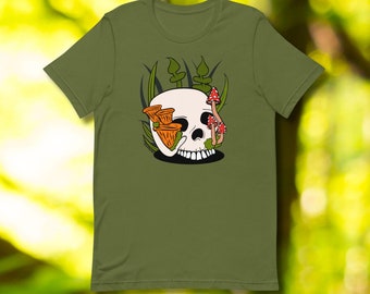 Op de afbeelding: Een groen T-shirt met een witte schedel omringd door oranje en rode paddenstoelen. De schedel is omringd door groene bladeren.