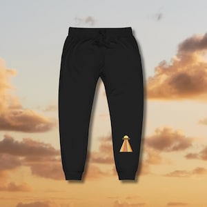 Könnte beinhalten: Schwarze Jogginghose mit einem bunten Grafikdruck eines UFOs auf dem linken Bein.