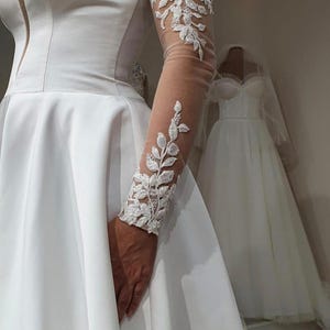 May include: A white strapless wedding dress with a full skirt and a lace overlay on the sleeves. The dress is made of a satin-like fabric and has a fitted bodice.