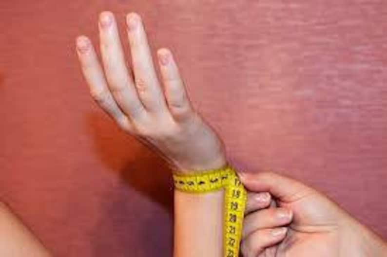 May include: A yellow measuring tape wrapped around a person's wrist to measure the circumference.