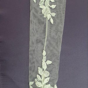 May include: White lace bridal gloves with floral embroidery. The gloves are sheer and delicate, with a floral pattern that extends from the wrist to the fingertips.