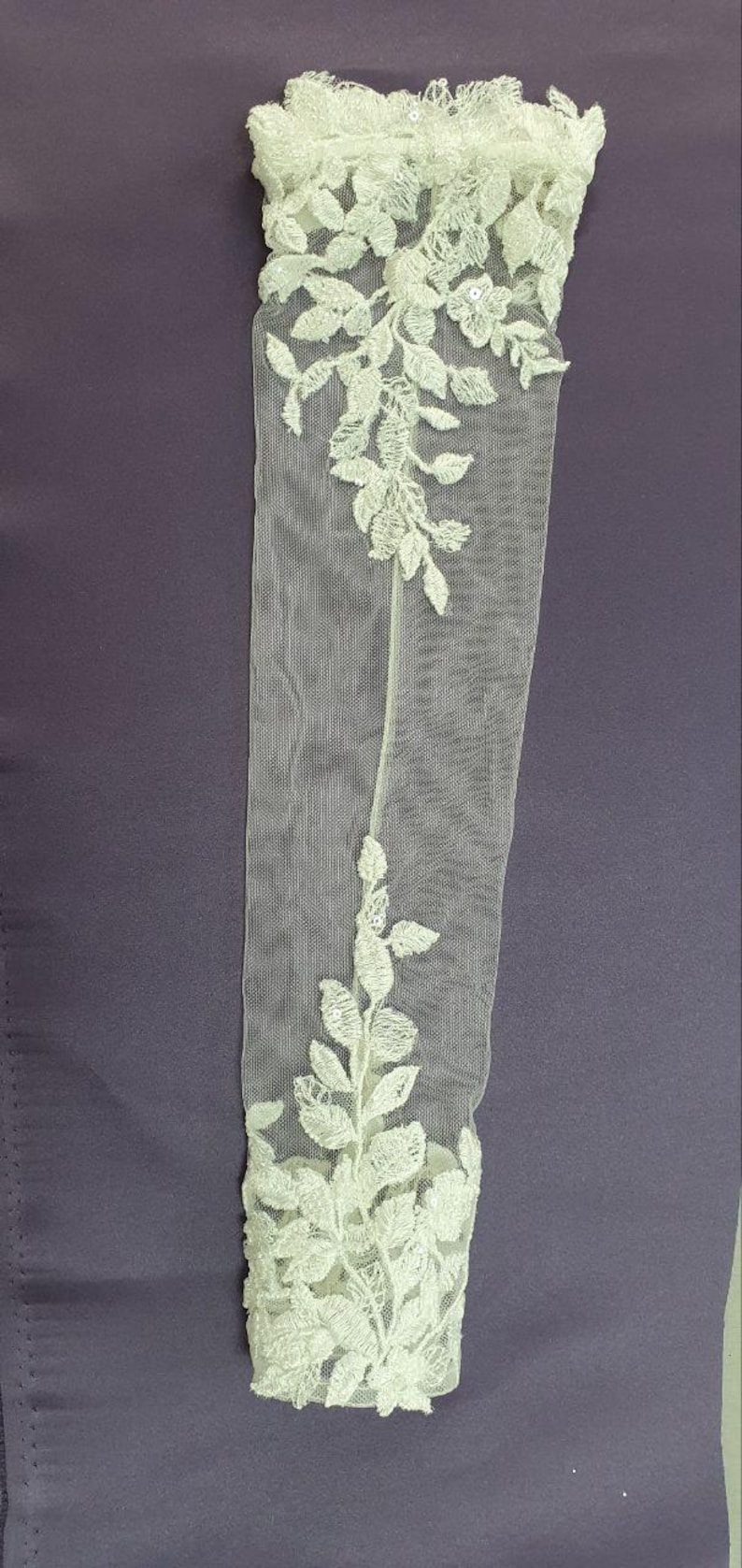 May include: White lace bridal gloves with floral embroidery. The gloves are sheer and delicate, with a floral pattern that extends from the wrist to the fingertips.