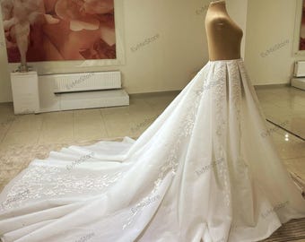 Puede incluir: Un vestido de novia blanco con una larga cola y delicados detalles de encaje. El vestido tiene un corpiño ajustado y una falda fluida.
