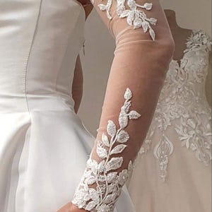 May include: White bridal lace sleeves with floral embroidery. The sleeves are sheer and have a delicate design.