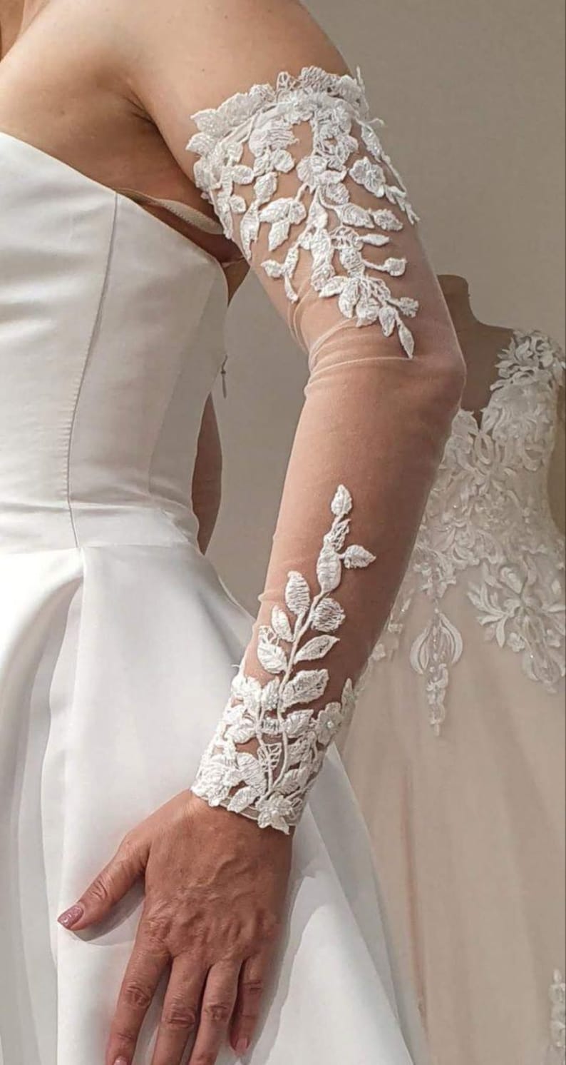 May include: White bridal lace sleeves with floral embroidery. The sleeves are sheer and have a delicate design.
