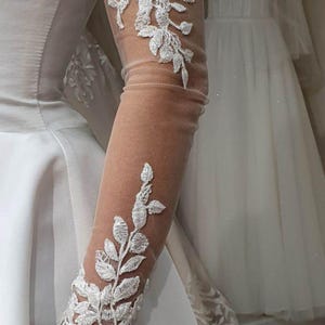 May include: White lace bridal gloves with floral embroidery. The gloves are sheer and extend to the elbow.