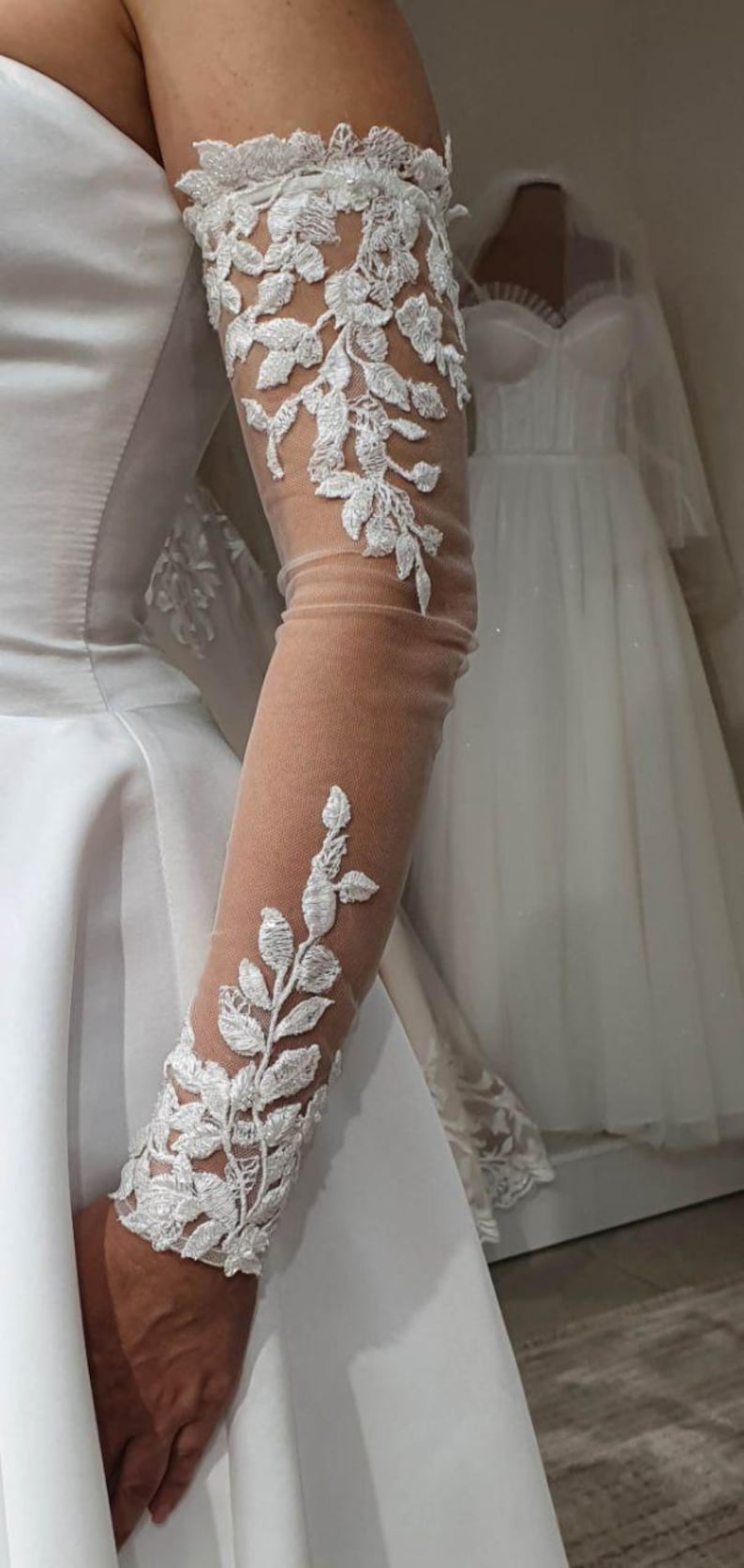 May include: White lace bridal gloves with floral embroidery. The gloves are sheer and extend to the elbow.