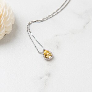 Pu&ograve; includere: Una collana a catena d'argento con un ciondolo a forma di pera in pietra preziosa gialla circondato da piccole pietre preziose trasparenti.