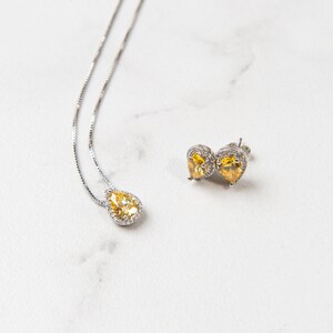 Pu&ograve; includere: Un set di collana e orecchini in argento con pietre gialle a forma di pera circondate da pietre trasparenti pi&ugrave; piccole.