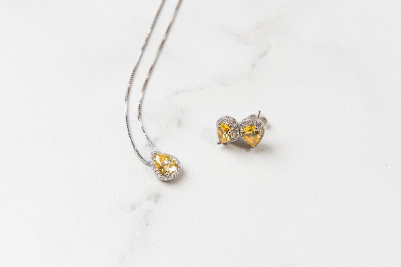 Pu&ograve; includere: Un set di collana e orecchini in argento con pietre gialle a forma di pera circondate da pietre trasparenti pi&ugrave; piccole.