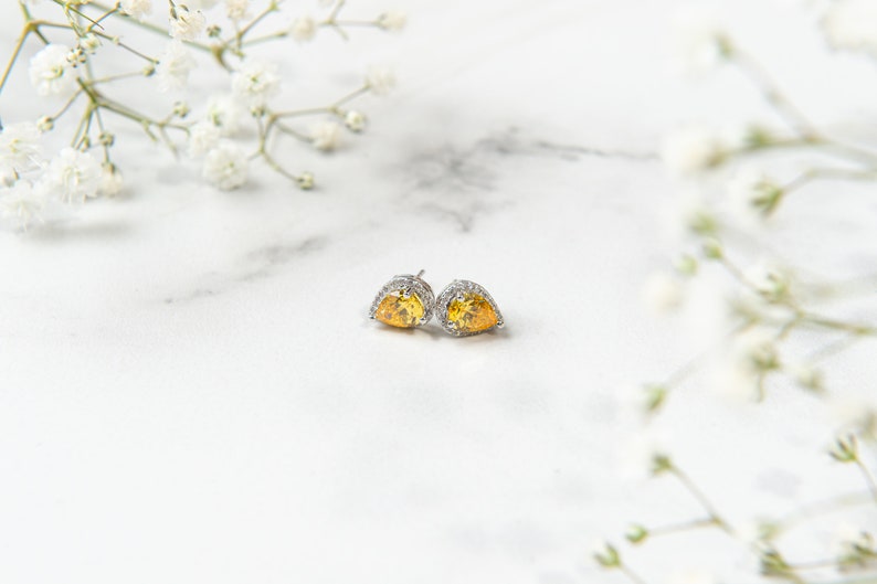 Pu&ograve; includere: Un paio di orecchini a forma di cuore in argento con una pietra preziosa gialla al centro e un'aureola di piccole pietre preziose chiare.
