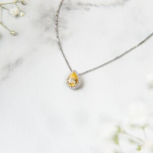Pu&ograve; includere: Una collana con catena d'argento con un ciondolo a forma di lacrima con una pietra preziosa gialla circondata da piccole pietre preziose trasparenti.