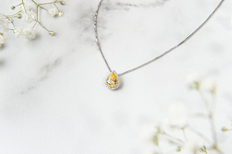 Pu&ograve; includere: Una collana con catena d'argento con un ciondolo a forma di lacrima con una pietra preziosa gialla circondata da piccole pietre preziose trasparenti.
