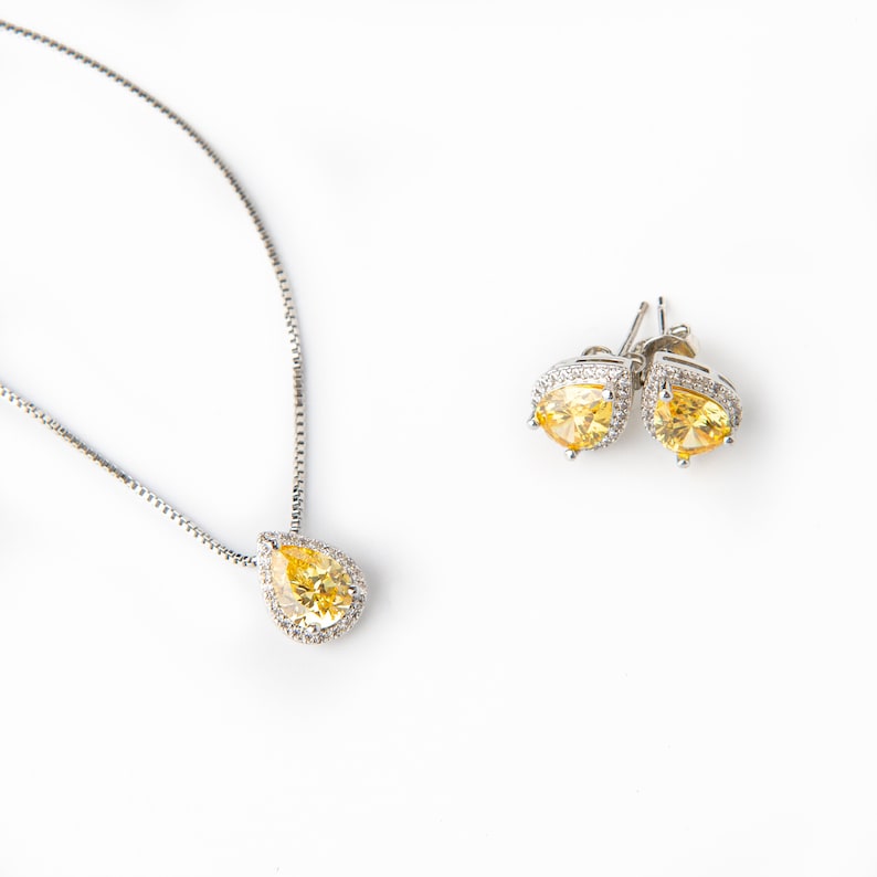 Pu&ograve; includere: Un set di collana e orecchini in argento con una pietra gialla a forma di lacrima circondata da pietre trasparenti pi&ugrave; piccole.
