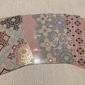 Może przedstawiać: Sześć ozdobnych zakładek do planera lub notesu. Zakładki mają powtarzający się wzór różowych i szarych kształtów geometrycznych z metalicznym złotym akcentem.