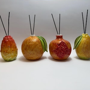Può includere: Quattro diffusori a bastoncino in ceramica a forma di frutta: un fico d'India, un'arancia, un melograno e una pera. Ognuno ha un bastoncino nero ed è dipinto con colori vivaci. Il melograno è aperto, rivelando semi rossi.