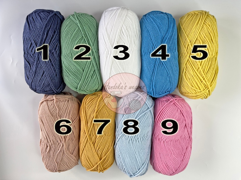 K&ouml;nnte beinhalten: Neun Garnkn&auml;uel in zwei Reihen angeordnet, nummeriert von eins bis neun. Die Farben umfassen Marineblau, Salbeigr&uuml;n, Wei&szlig;, Blau, Gelb, Beige, Senfgelb, Hellblau und Rosa. Ein kreisf&ouml;rmiges Logo mit dem Text Handoka's weaves ist zu sehen.