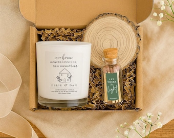 May include: A gift box containing a white aromatherapy candle with text, a wooden slice, and a small glass bottle of matches. The candle has the words "New Home, New Beginnings, New Memories" and the names "Ellie & Dan". The match bottle says "Let There Be Light".
