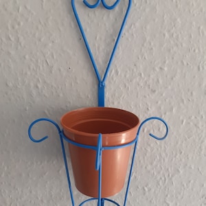 May include: Blue metal plant hanger with a heart-shaped design. The hanger has a round base and a pot holder.