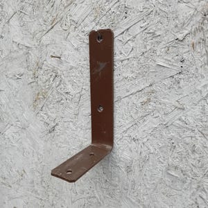 May include: A brown metal L-bracket with two holes on the vertical side and one on the horizontal side. The bracket is designed for structural support and is made of durable metal.