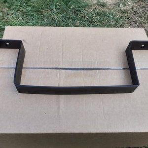 May include: Black metal shelf bracket with two mounting holes on each side. The bracket is sitting on a brown cardboard box.