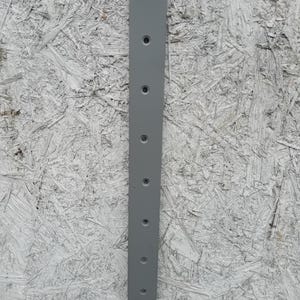 May include: A grey metal plate with eight evenly spaced holes drilled into it. The plate is rectangular and has a smooth, matte finish.