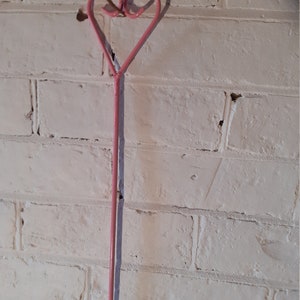 May include: A pink metal heart-shaped wall decoration. The heart is made from a single piece of bent metal and is mounted on a white painted brick wall. The heart's shadow is visible on the wall.
