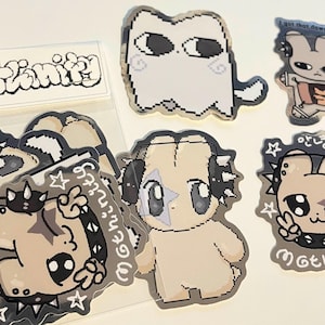 May include: A collection of stickers featuring pixelated cartoon characters in various poses. The stickers have a neutral color palette with black accents and text that reads "mothinity". Some stickers have a star and peace sign.
