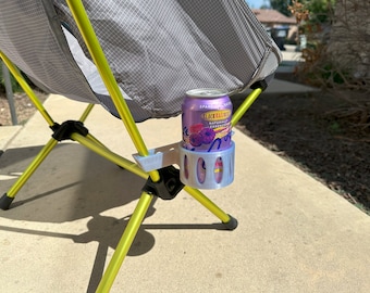 May include: A grey and yellow camping chair with a 3D printed grey cup holder attached to one of the legs. A purple can of Black Raspberry Sparkling Essence is in the cup holder.