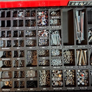 May include: A black plastic drawer organiser tray filled with various metal hardware components including washers, nuts, and bolts. Each compartment is labelled with specific sizes such as M3, M4, M5, M6, M8, M10, M12, #8-32, #10-24, 1/4-20, 3/8-16, and 5/16-18.