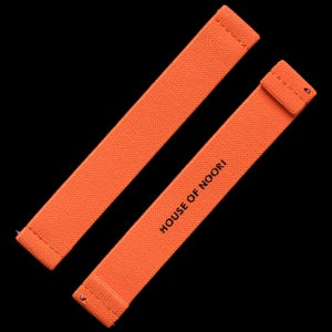 Pode incluir: Duas pulseiras de relógio de tecido laranja com detalhes de costura. A pulseira de baixo tem o texto "HOUSE OF NOORI" impresso.