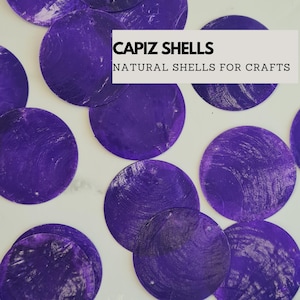 May include: Purple capiz shells, a natural material used for crafts. The shells are round and have a slightly iridescent sheen.