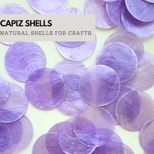 Puede incluir: Primer plano de un montón de conchas capiz de color púrpura. Las conchas son redondas y tienen un brillo nacarado. El texto "CAPIZ SHELLS NATURAL SHELLS FOR CRAFTS" es visible en la parte superior de la imagen.