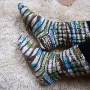 Könnte beinhalten: Ein Paar bunte gestreifte Socken mit grünen, blauen, weißen und braunen Streifen. Die Socken sind aus weichem, gestricktem Stoff.