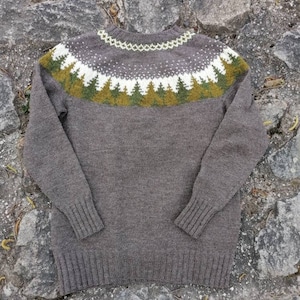 May include: A brown knitted sweater with a green, white, and brown patterned yoke. The yoke features a design of stylized pine trees.