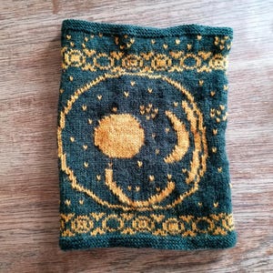 May include: A knitted green and gold neck warmer with a moon and sun design.