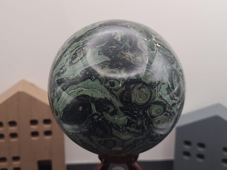 May include: A green and black sphere with swirling patterns, made of polished stone. The sphere is on a wooden stand.