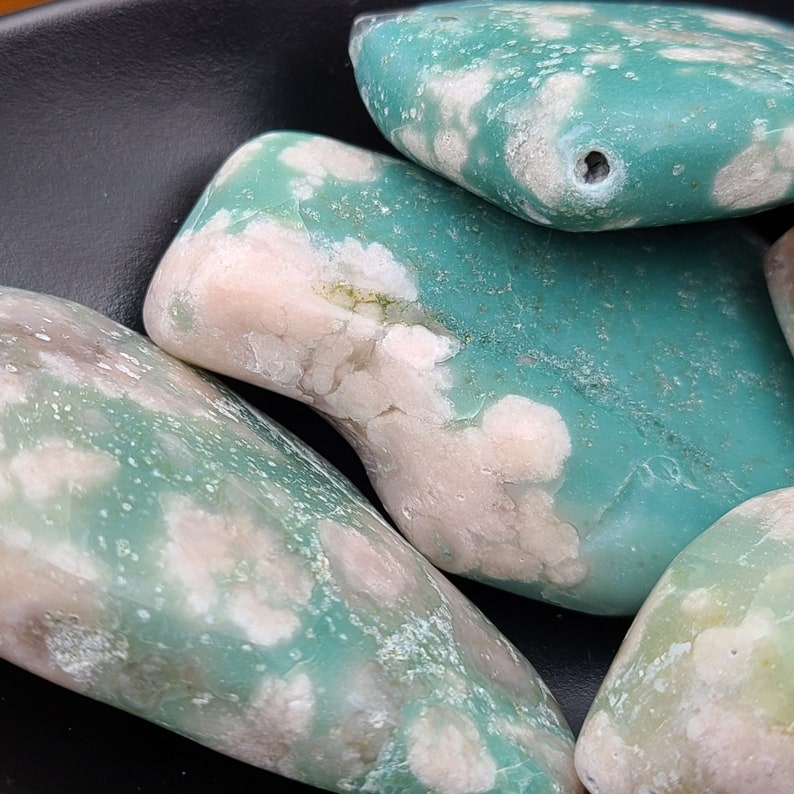 May include: Close-up of three smooth, polished stones with a mottled green and white pattern. The stones have a natural, organic shape and a glossy finish.