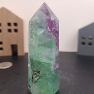 May include: A green and purple fluorite crystal point with a pointed tip and a flat base. The crystal is translucent and has a variety of colors, including green, purple, and white.