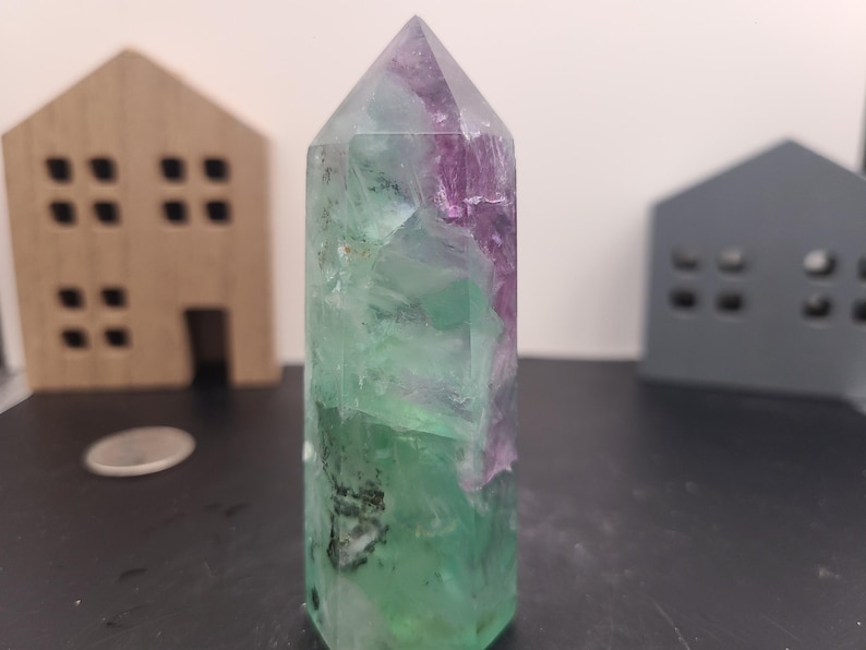 May include: A green and purple fluorite crystal point with a pointed tip and a flat base. The crystal is translucent and has a variety of colors, including green, purple, and white.