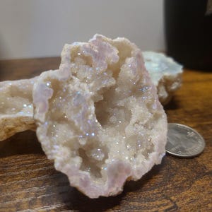 May include: A white geode with iridescent crystals inside. The geode is open and the crystals are visible. The geode is on a wooden surface.