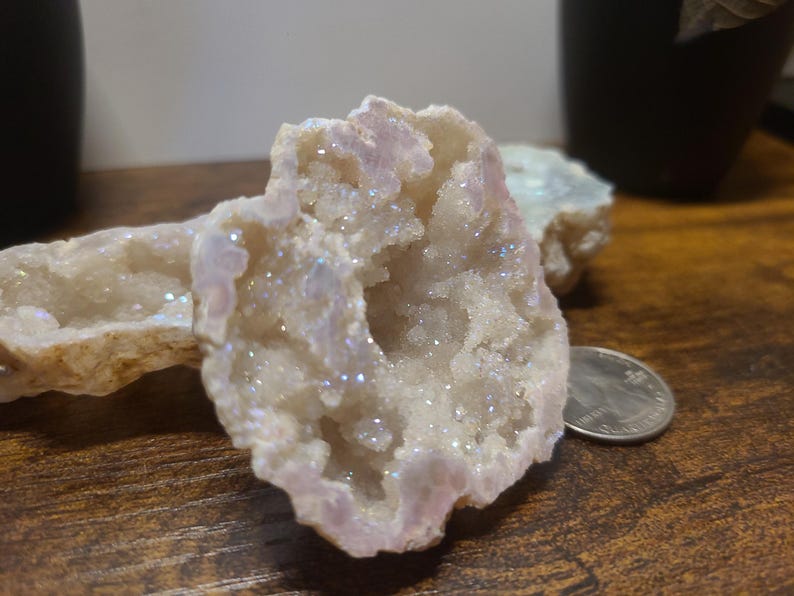May include: A white geode with iridescent crystals inside. The geode is open and the crystals are visible. The geode is on a wooden surface.