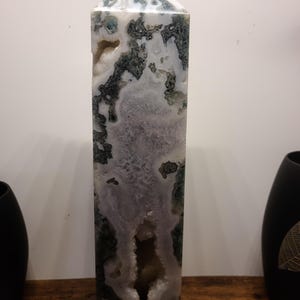 May include: A tall, white, green, and purple agate crystal point with a large, open cavity. The crystal is polished and has a smooth, glassy surface.